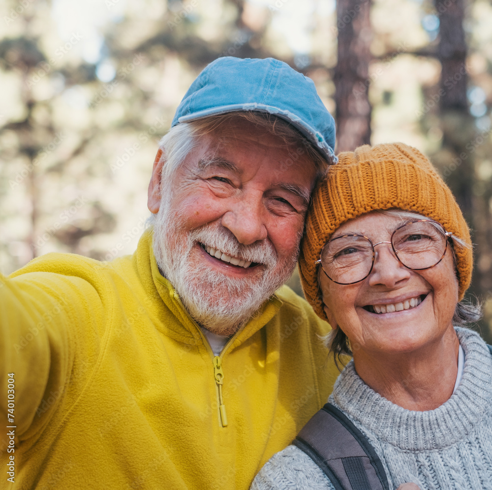 Head shot portrait close up of cute couple of old seniors taking a selfie together in the mountain forest looking at the camera smiling having fun enjoying. Two mature people hiking.